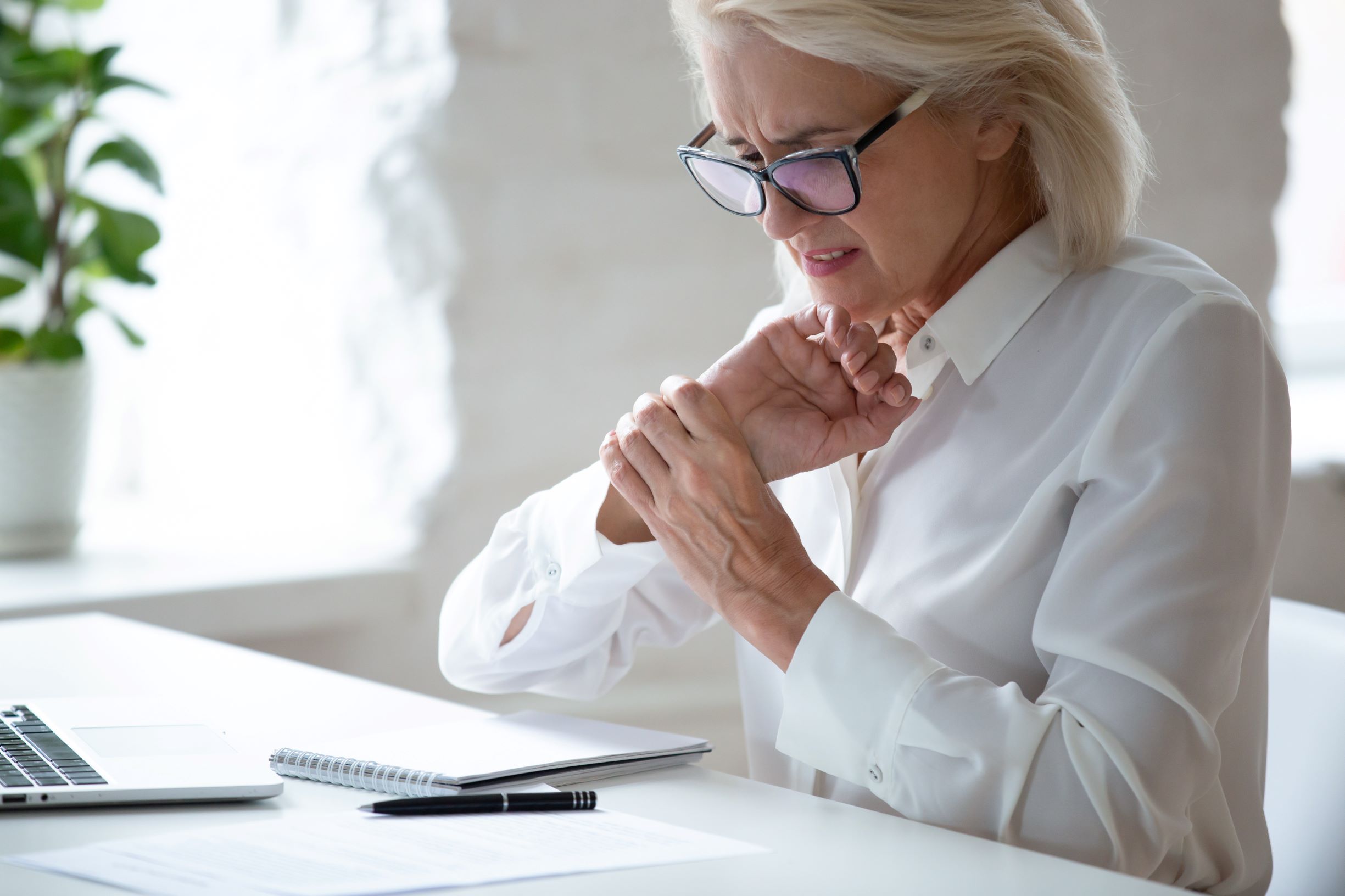 Woman experience hand and wrist nerve pain while working at desk with computer and notepad.